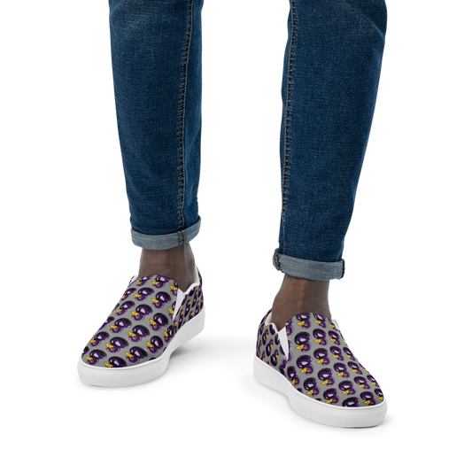 closeup view of man in jeans wearing mens slip-on canvas shoes with a black and purple rubber duck logo pattern over gray background