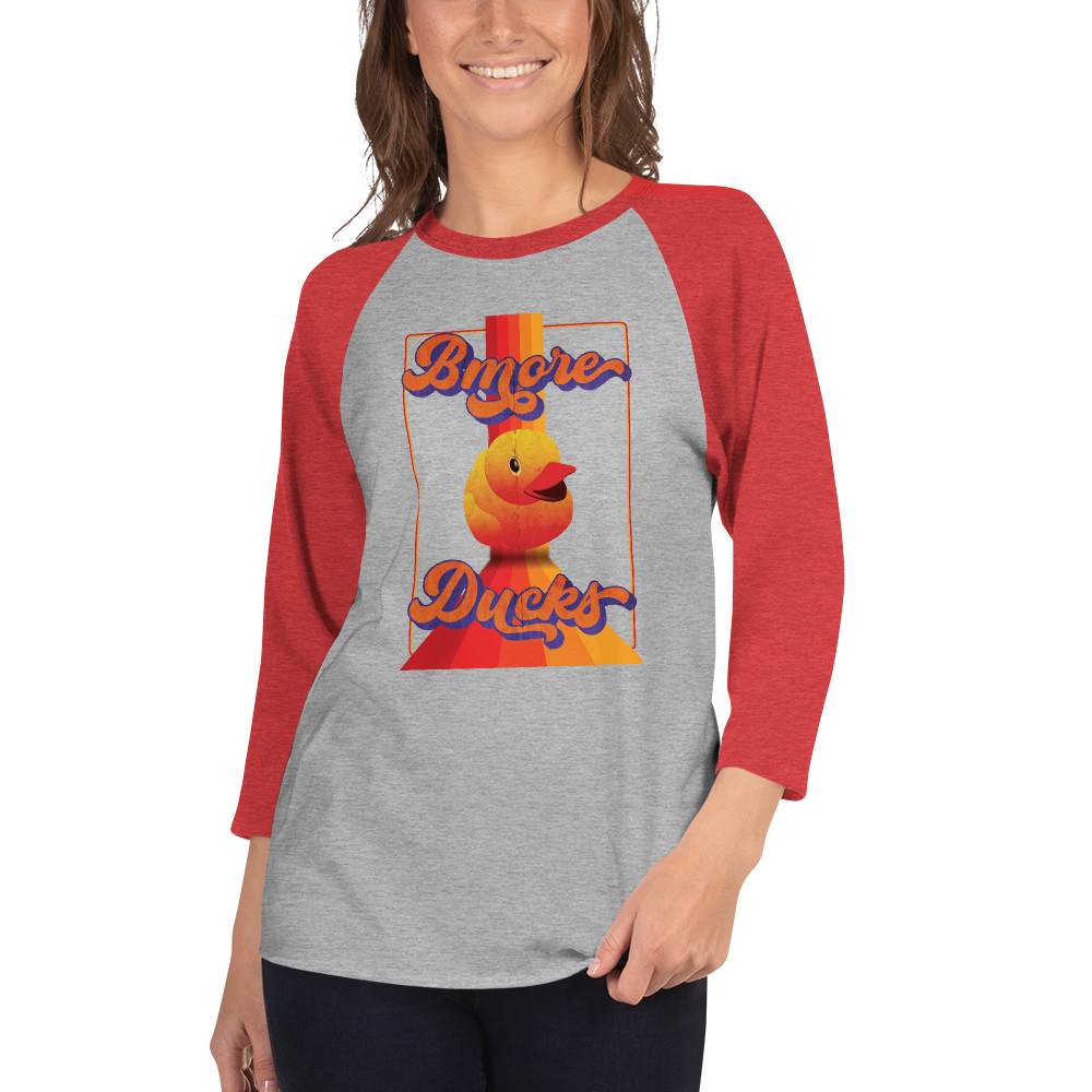 woman wearing a red sleeve, gray centered raglan shirt with a vintage 1970's design that says "Bmore Ducks" and features a yellow rubber duck