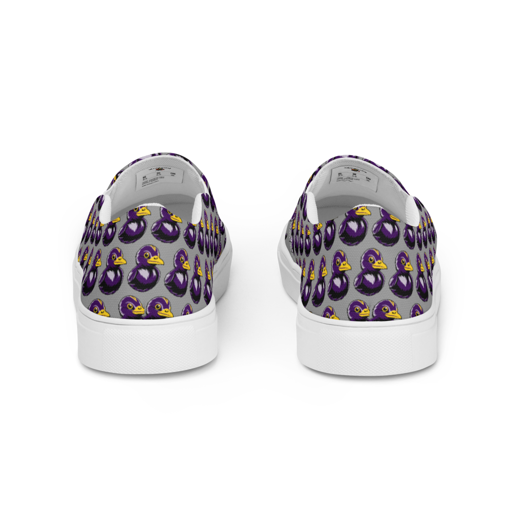 rear view of mens slip-on canvas shoes with a black and purple rubber duck logo pattern over gray background