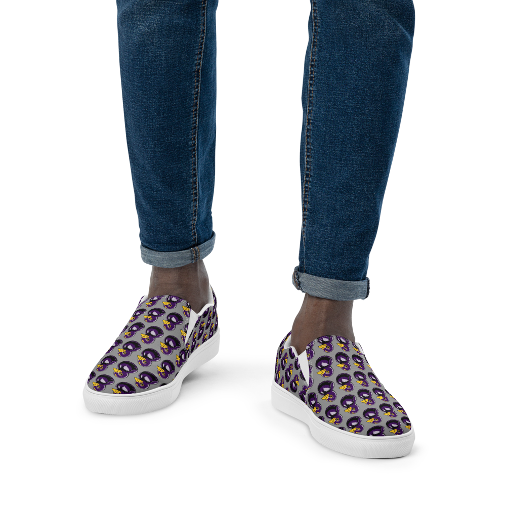 closeup view of man in jeans wearing mens slip-on canvas shoes with a black and purple rubber duck logo pattern over gray background