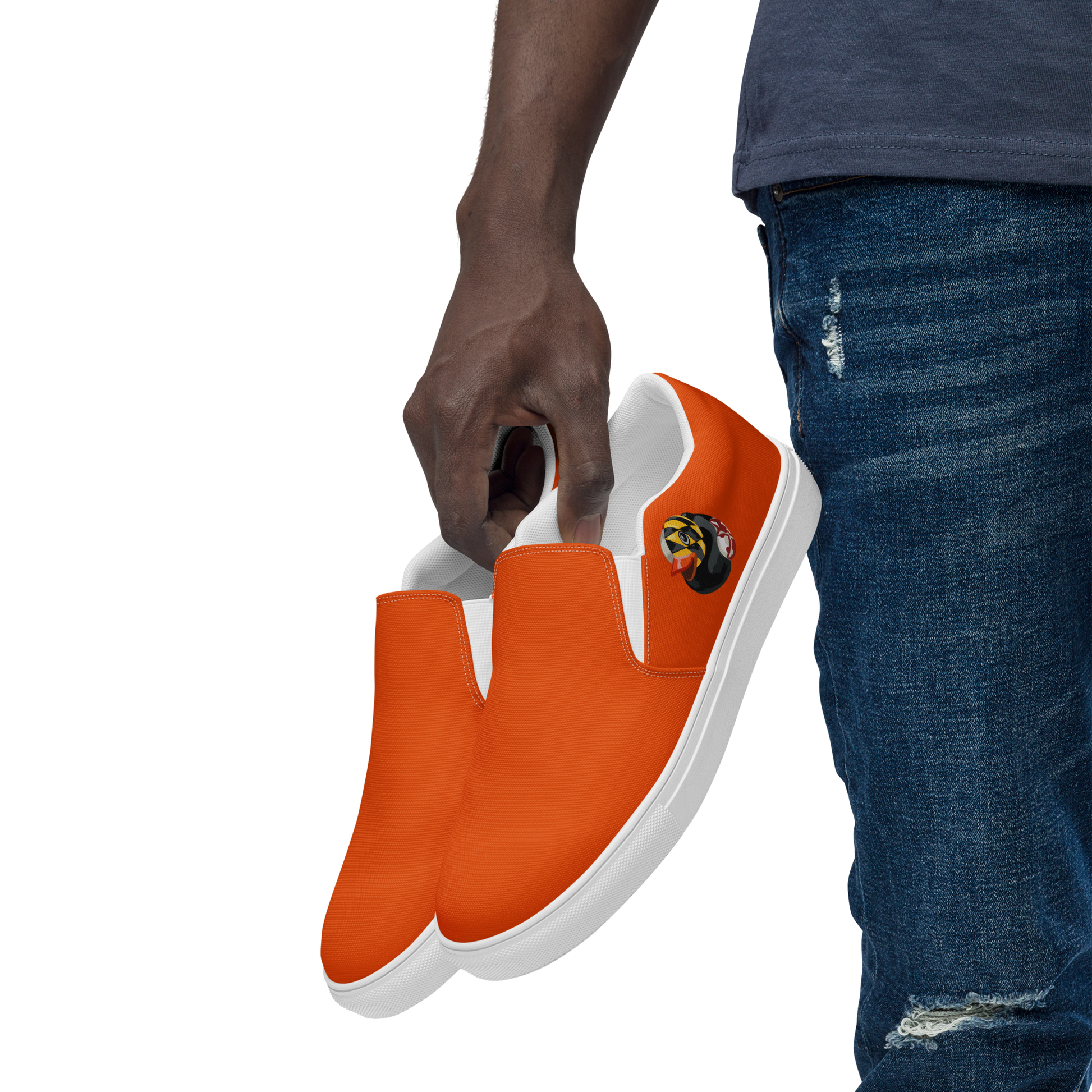 Photo of man holding by his side, a pair or orange BMORE DUCKS! mens slip on canvas shoes