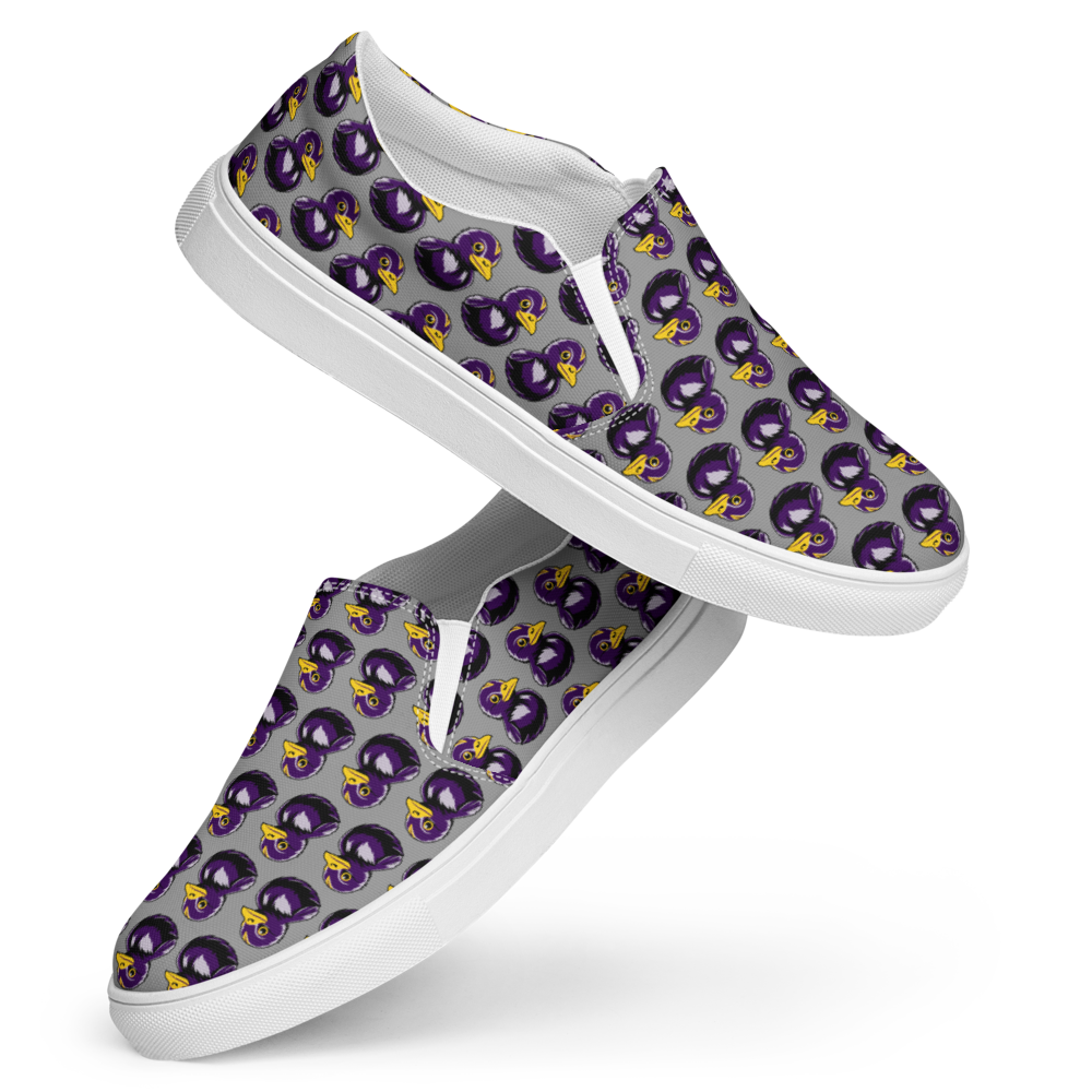 side view of right shoe over left shoe of womens canvas slip on shoes featuring a rubber duck in black and purple over gray background