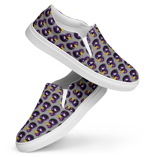 side view of right shoe over left shoe of womens canvas slip on shoes featuring a rubber duck in black and purple over gray background